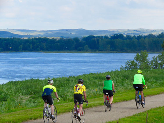 Cyclists riding by Double Ditch Indian Village State Historic site with the Missouri River in the background