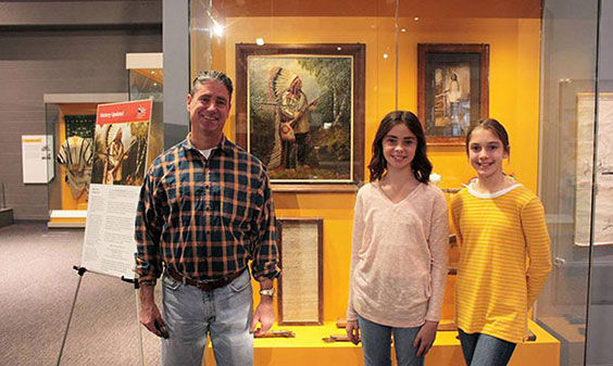 Man and two young girls standing in front of Sitting Bull painting