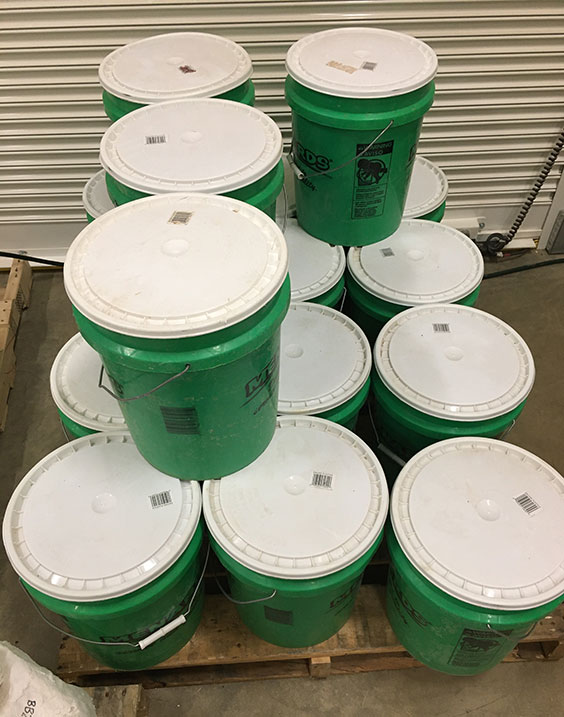 Many green buckets with white lids sit stacked on a pallet.