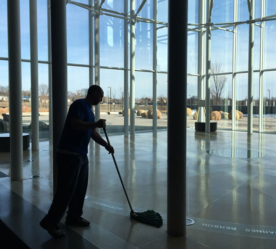 A man mops the floor in a room shaped like a box with all glass windows.