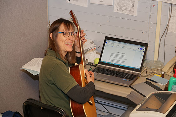 Kris sitting with a guitar in hands and computer in front of her