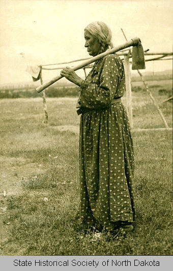 Scattered Corn standing outside holding a hoe over her shoulder