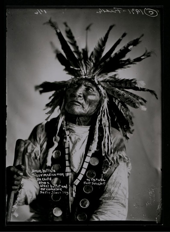 Photo of Brave Buffalo wearing headdress and vest.