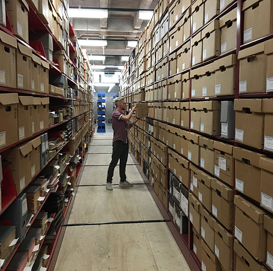 College-aged man standing in an isle of shelves full of boxes